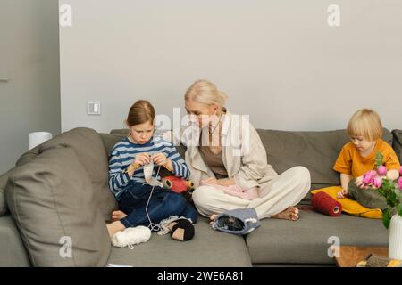 Nonna seduta con i nipoti che lavorano a maglia sul divano a casa Foto Stock