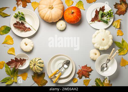 Varie zucche colorate, foglie autunnali e piatti vuoti con posate per il Ringraziamento Foto Stock