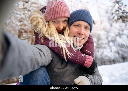 Un uomo maturo sorridente che fa selfie con una figlia nella foresta di neve Foto Stock