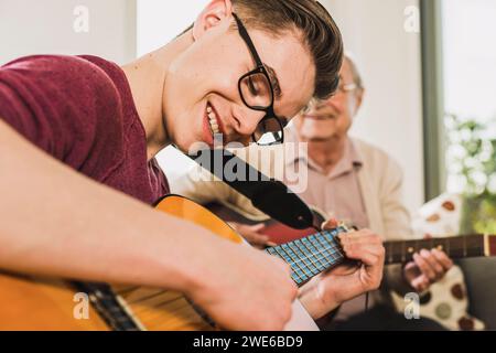 Felice giovane che suona la chitarra con il nonno a casa Foto Stock