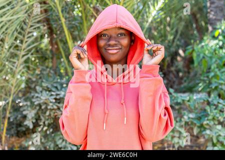 Giovane donna sorridente che indossa una camicia rosa con cappuccio al parco Foto Stock