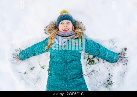 Ragazza felice sdraiata sulla schiena e facendo angelo di neve Foto Stock
