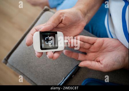 Mani di donne che usano glucometro a casa Foto Stock