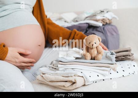 Donna incinta seduta con orsacchiotto imbottito e vestiti da imballaggio a casa Foto Stock