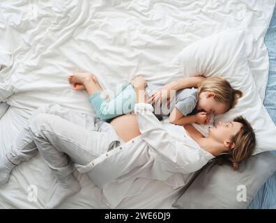 Madre incinta sdraiata con figlia a letto a casa Foto Stock