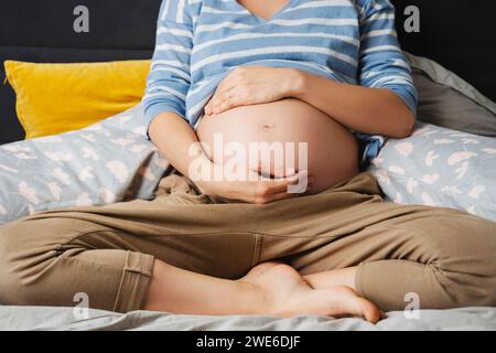 Donna incinta seduta a letto a casa Foto Stock