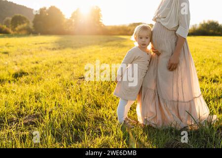 Figlia appoggiata allo stomaco della madre incinta sul campo Foto Stock