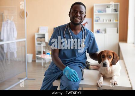 Veterinario sorridente seduto con il cane beagle sul tavolo della clinica Foto Stock