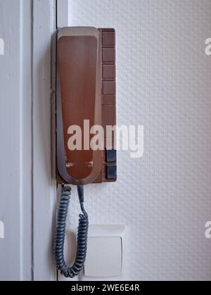 Telefono da parete marrone vintage, appeso a una parete ruvida bianca. Il telefono dispone anche di interfono inferiore per consentire alle persone di entrare nella porta d'ingresso Foto Stock