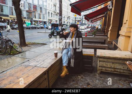Donna che si gusta la pizza al caffè sul marciapiede di fronte agli edifici Foto Stock