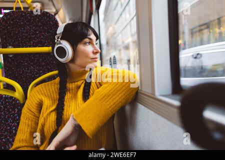 Donna premurosa che indossa cuffie wireless e siede in autobus Foto Stock