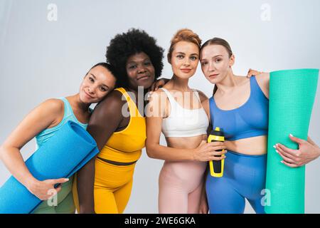 Amici femminili multirazziali con tappetini per yoga e bottiglia d'acqua su sfondo bianco Foto Stock