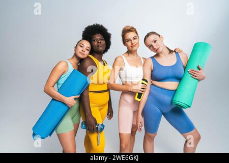 Amici femminili multirazziali con tappetini da yoga e bottiglie d'acqua su sfondo bianco Foto Stock