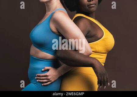 Giovani donne in piedi da una parte all'altra con braccio in braccio su sfondo marrone Foto Stock