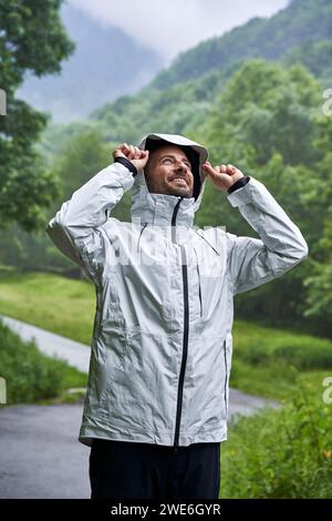 Uomo felice che indossa una giacca bianca e si trova di fronte alla montagna Foto Stock