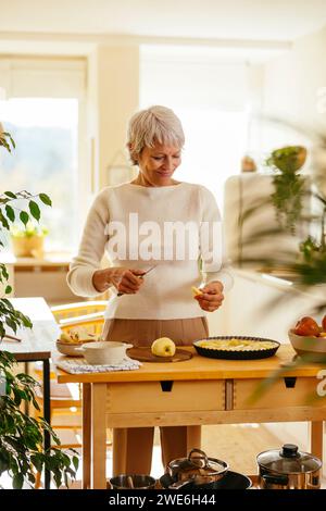 Donna felice che taglia le mele per la torta in cucina Foto Stock