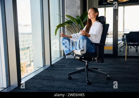 Donna d'affari sorridente che pratica meditazione sulla sedia da ufficio Foto Stock
