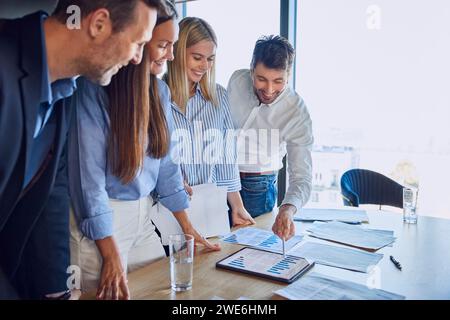 Uomo d'affari felice che discute di grafici e dati con i colleghi alla scrivania Foto Stock