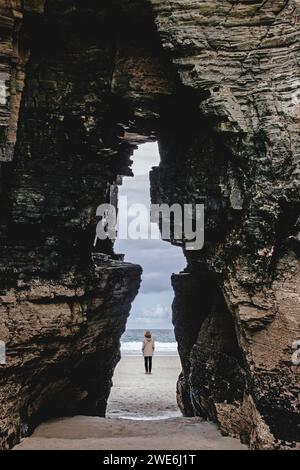 Donna matura in spiaggia vicino alla formazione rocciosa Foto Stock