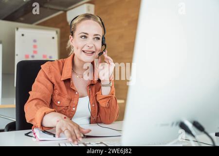 Donna d'affari sorridente che indossa cuffie e partecipa a una videoconferenza Foto Stock