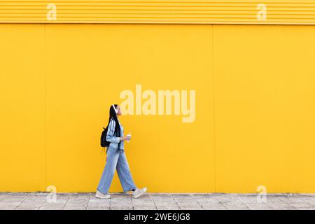 Giovane donna che cammina su un sentiero di fronte al muro giallo Foto Stock