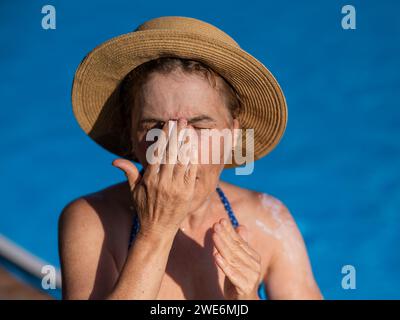 Ritratto di una donna anziana che applica la crema solare al viso mentre è in vacanza. Foto Stock