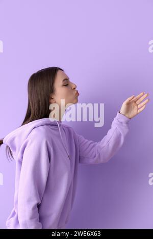 Giovane donna che lancia un bacio su sfondo lilla Foto Stock