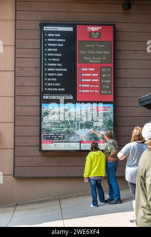 I turisti che guardano un cartello che mostra la mappa, le condizioni meteorologiche e lo stato degli ascensori Jackson Hole Aerial tram station a Teton Village, Jackson, Wyoming Foto Stock