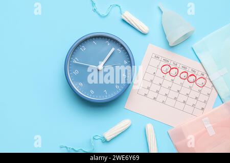 Composizione con calendario mestruale, diversi prodotti per l'igiene femminile e sveglia su sfondo colorato Foto Stock