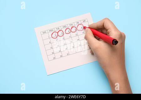 Donna che segna il suo periodo nel calendario mestruale su sfondo colorato Foto Stock