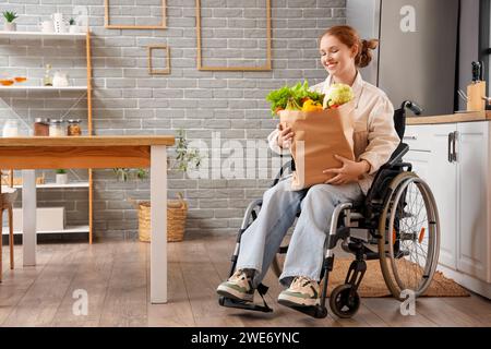 Giovane donna rossa in sedia a rotelle con sacchetto di carta di cibo sano a casa Foto Stock