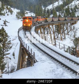 il treno che trasporta le carrozze a carbone verso mullan passa sopra un cavalletto in inverno vicino ad austin, montana Foto Stock