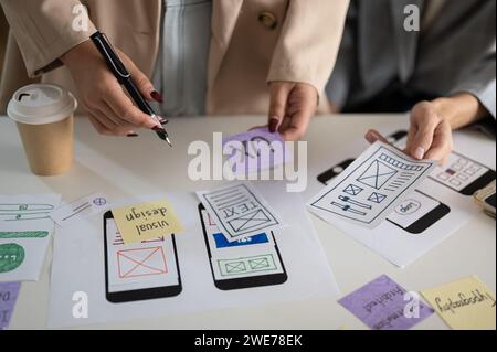 Una foto ritagliata di un gruppo di grafici UX e UI che lavorano e fanno brainstorming su una nuova progettazione di applicazioni mobili durante la riunione. uomini d'affari c Foto Stock