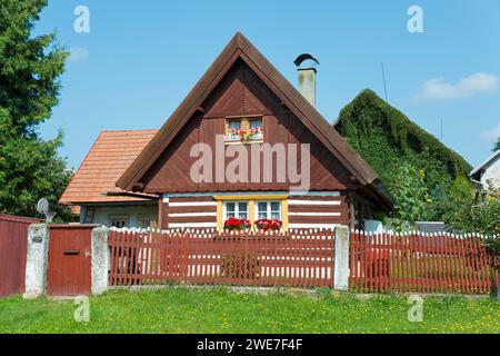 Piccolo cottage con tetto rosso e persiane bianche, circondato da un giardino e una recinzione in legno, vecchia casa in legno, Vesec u Sobotky, conservazione del villaggio Foto Stock