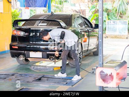 Misurazione da parte del tecnico delle emissioni di scarico presso la stazione di ispezione tecnica. Un riparatore di automobili applica una sonda allo scarico. Foto Stock
