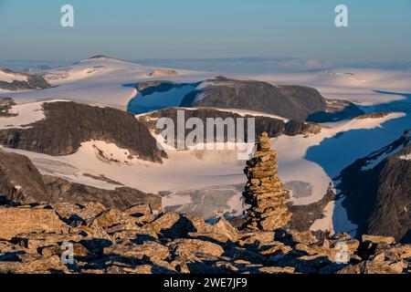 Cairn sulla cima di Skala, luce calda al tramonto, cima e ghiacciaio Jostedalsbreen sullo sfondo, Loen, Norvegia Foto Stock