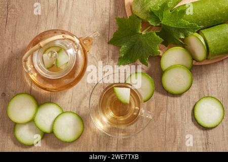 Su un tavolo di legno, una teiera trasparente e una tazza riempita di tè al melone invernale esposta con un vassoio di melone fresco invernale. Melone invernale (Benincasa hisp Foto Stock