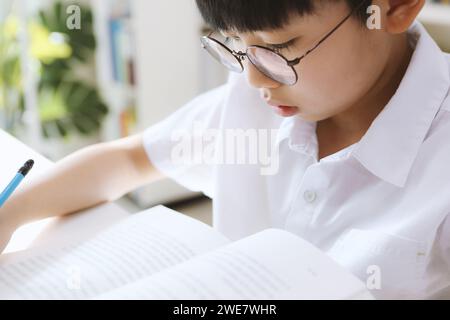 Un bambino intelligente che indossa gli occhiali si sta concentrando sulla lettura e sullo studio, tenendo una matita in mano e imparando. Foto Stock