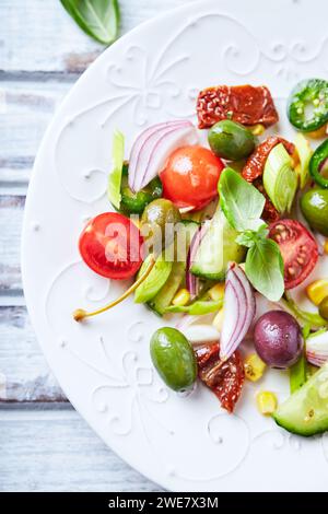 Insalata semplice con olive verdi e calamata, cetrioli, ciliegie e pomodori marinati, Capperi e pepe jalapeno. Sfondo in legno luminoso. Vista dall'alto Foto Stock