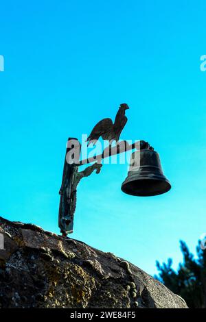 Una campana di metallo con gallo contro il cielo blu Foto Stock