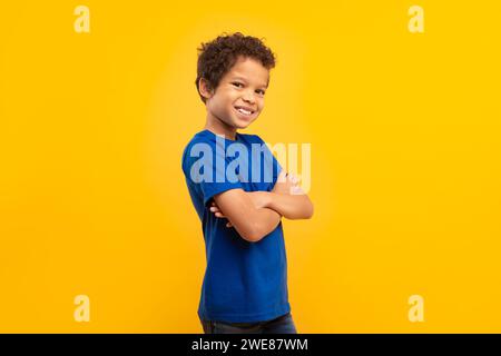 Ragazzo sicuro di sé con le braccia incrociate in camicia blu su sfondo giallo Foto Stock