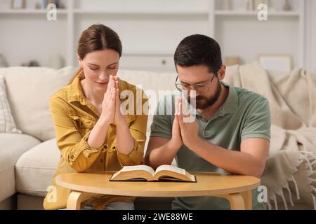 Coppia di famiglie che pregano per la Bibbia insieme a un tavolo al chiuso Foto Stock