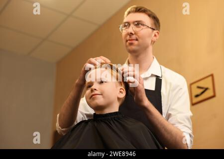 Parrucchiere professionale che lavora con il ragazzo in un salone di bellezza, con vista dall'angolo basso Foto Stock