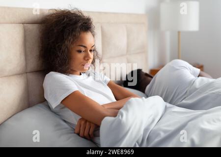 Donna nera infelice seduta accanto al marito addormentato a letto Foto Stock