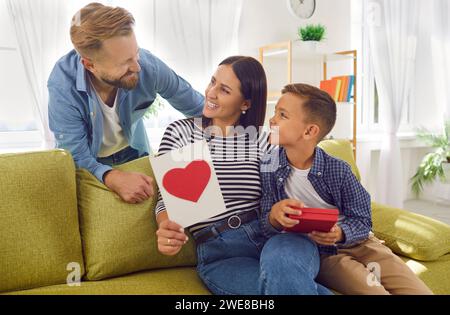 La bella e felice donna riceve un regalo dall'amore di marito e figlio per la festa della mamma Foto Stock