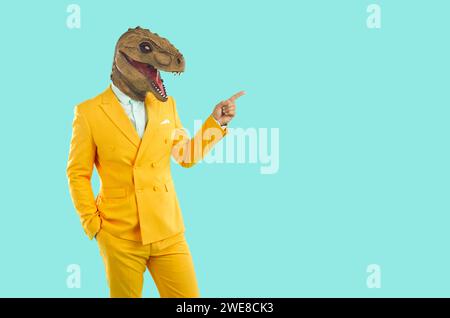 Elegante uomo con una divertente maschera di dinosauro, punta a uno spazio vuoto da copiare. Foto Stock