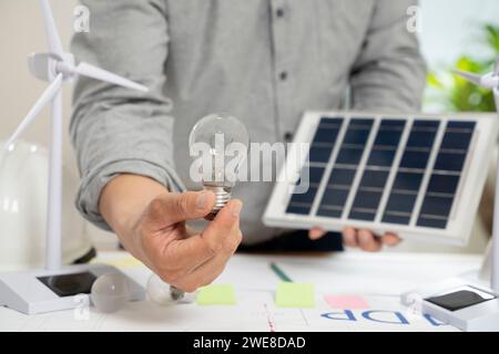 Uomo d'affari che tiene pannelli solari e lampadine in ufficio. Foto Stock