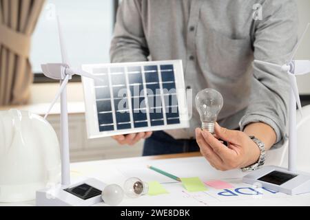 Uomo d'affari che tiene pannelli solari e lampadine in ufficio. Foto Stock