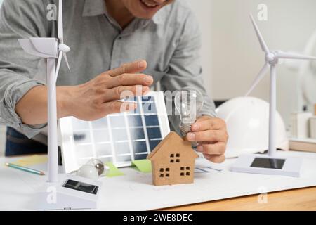 Uomo d'affari che tiene pannelli solari e lampadine in ufficio. Foto Stock