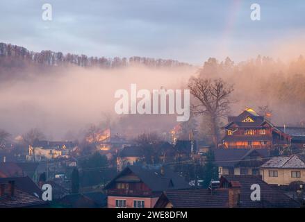 Un piccolo villaggio nebbioso avvolto dalla nebbia e circondato da alberi lussureggianti al mattino Foto Stock
